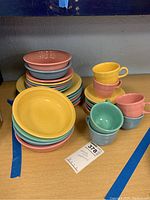 Photo showing the full collection of Fiesta Ware plates, bowls, and cups stacked in multiple colors of yellow, pink, blue and green hues.
