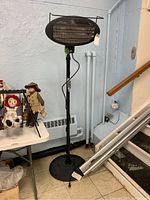 Front full view of the Vivian Home heat lamp on stand near wall and table with dolls.