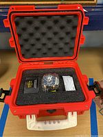 View of open red hard protective case containing the plastic wrapped Invicta Marvel watch, instruction manual, and warranty card set in foam insert.