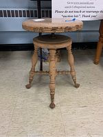 Front angled view of the adjustable piano stool showing round seat with paint chipping and carved legs ending in claw feet on castors.