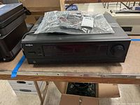 Front and top view of Insignia NS-R2000 AM/FM stereo receiver with remote control on top in plastic bag.