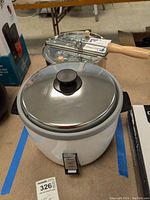 Full view of the Oster rice cooker with stainless steel lid in white body, showing front switch detailing.