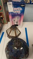 Sparkle Lamp packaging with two stained glass lamp shades (blue and amber) in foreground