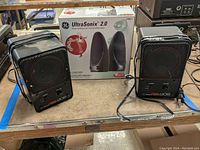 Pair of black rectangular Fostex 6301B monitor speakers with power cords alongside boxed GE UltraSonix 2.0 speakers