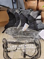 Four Stohlquist adult life jackets lined up with a clear mesh storage bag in front