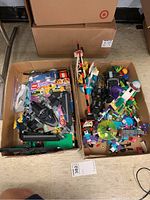 Two open cardboard boxes on floor filled with assorted LEGO pieces and some instruction books