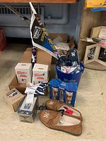 Wide view of lot showing all items grouped on floor including steins, bucket with mug and flags, trading cards, slippers, towel, and flip flops