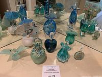 The full lot of various blue and green glass perfume bottles and decorative glass objects displayed in front of a mirror.