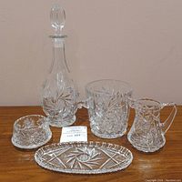 Overview of the 5-piece cut crystal glass set showing decanter with stopper, ice bucket, creamer, sugar bowl, and tray all on a wooden surface against beige wall.