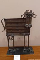 Full front view of whimsical metal cow sculpture showing body, legs, tail and base.