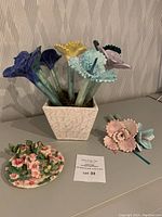 Ceramic pot with 7 tall flowers, small plate with pink flowers, two-flower bouquet, and hummingbirds arranged on table