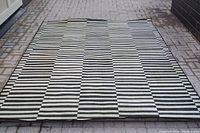Full view of large black and white striped rug laid out on patio stones, showing overall size and pattern.