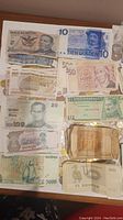 Photo of multiple international banknotes from Mexico, Netherlands, Venezuela, Thailand, Tanzania, and other countries, showcasing various denominations and portraits.