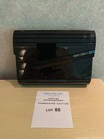 Front view of black acrylic clutch showing stepped geometric detailing and angled accent bar with logo