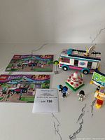 Photo showing the assembled Heartlake News Van, two mini-figures, accessories including cake and camera, and instruction booklets.