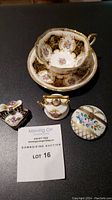 Photo showing Paragon fine china floral tea cup and saucer alongside three hand-painted Limoges miniature trinket boxes shaped like a teapot, basket, and handbag.