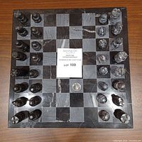 Top-down image of the full chess set on the board showing black and grey marble squares and all chess pieces arranged in starting positions