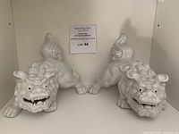 Front view of the pair of white porcelain foo dogs, displaying their faces and front paws.