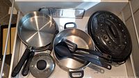 Image of stainless steel pots and frying pans, black speckled roasting pan, and black plastic utensils in drawer