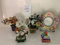 Photo of entire lot showing three small jade bonsai trees, a colorful crystal paperweight pyramid, and a flower-shaped picture frame with floral decoration.