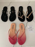 Top down photo showing all three pairs of flip flops on a white marble-like surface, from black with scalloped strap, black with metallic pink gold and white gold straps to pink ombre pair.