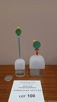 Pair of frosted glass Art Deco style perfume bottles with distinctive colored necks and decorative stoppers shown side by side with a coin for scale.