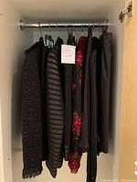 Overview of six garments hanging on rack: fringe-trim jacket, striped blazer, red floral piece, and black skirts.