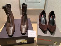 Both pairs of shoes presented on their original Prada boxes, showing the ankle boots on left and suede pumps on right.