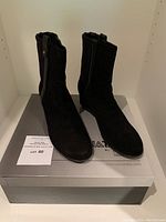 Front view of the black Aquatalia ankle boots on top of the shoebox with lot card visible.