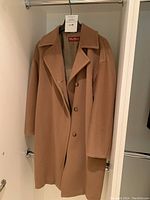 Front view of camel wool coat hanging on black hanger inside closet