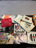 Photo showing an assortment of 45 RPM vinyl singles on a table, including notable covers such as We Are The World, Dancing in the Street, and others.
