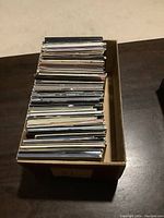 Box containing approximately 65 rock CDs in cardboard sleeves stacked vertically