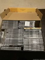 Overview photo of a box filled with stacked CD jewel cases showing spines and front covers of rock music singles and doubles.