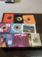 Top view showing multiple 45 rpm vinyl records with paper and original sleeves featuring various artists including The Rolling Stones and Doctor and the Medics.