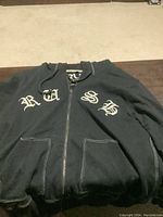 Front view of the black hoodie showing white Old English 'RUSH' embroidery on chest, zippered front, and pockets.