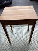 Front angled view of small wooden end table showing drawer and legs