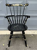 Front view of a black Windsor chair featuring gilt floral detailing on the top rail and armrests. Shows wear on seat.