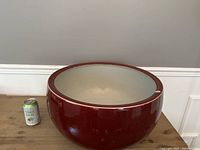 Full view of large oxblood red porcelain bowl with creamy white interior and a soda can for size reference.