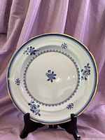 Full front view of the Copeland Spode collectible plate displayed on a stand against a purple draped background, showing blue floral decoration and gold rim.