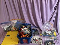 Wide shot showing the blue bins filled with assorted LEGO bricks, yellow baseplates on the side, and multiple smaller bags containing various additional LEGO parts and mini-figures.