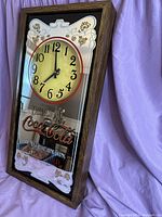 Full side angled view of the Coca Cola wall clock showing the wooden frame and mirrored face with clock face and branding.