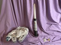 Millennium Falcon toy, lightsaber, and small character figures arranged on purple backdrop