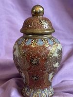 Front and side views of a small Satsuma lidded jar showing detailed hand-painted floral motifs, gold embellishments, and patterned background.