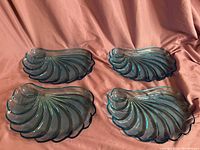 Four cornflower blue glass shell-shaped dishes arranged together on a satin-like fabric background, showing overall lot composition and color.