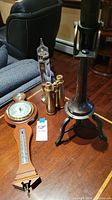 Full view of all three items: brass binoculars, brass telescope on tripod, and wooden barometer-thermometer on table.