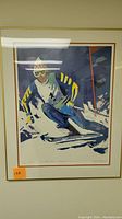Framed print showcasing a ski man with yellow and black striped jacket and goggles, vibrant blues and whites throughout the image.