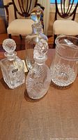 Four crystal glass items: three decanters with stoppers and one pitcher on wooden table.