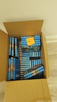 Box containing numerous Hardy Boys hardcover books with blue covers stacked neatly inside.