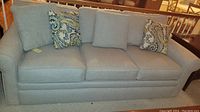Front view of beige three-seat La-Z-Boy sofa with three seat and back cushions and two paisley throw pillows