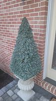 Full view of the artificial topiary tree in the decorative planter against a brick wall background.